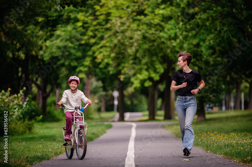 Wallpaper Mural Young mother in jeans and black t-shirt teaching and playing with her daughter in summer parks while girl riding a bike Torontodigital.ca