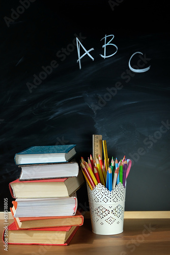 stack of books and stationery supplies on table, chalk blackboard background. Back to school, beginning of school year, start of education concept. Teacher\'s day. Knowledge Day. Template for design