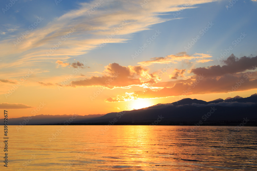Colorful sunset on the sea. Mountain lake in the rays of the orange sun. Kyrgyzstan, Lake Issyk-Kul.