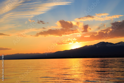 Colorful sunset on the sea. Mountain lake in the rays of the orange sun. Kyrgyzstan, Lake Issyk-Kul.
