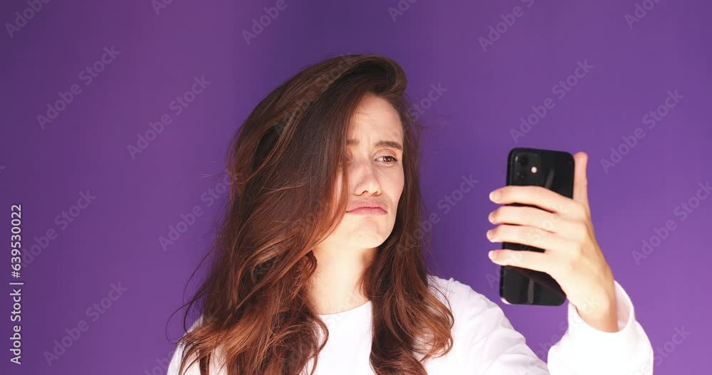 Close up young girl sad while read a message about broke up. Sad young woman isolated on purple background looking at smartphone screen and be melancholy after receiving bad news. Bad mood. Close up young girl sad while read a message about broke up. Sad young woman isolated on purple background looking at smartphone screen and be melancholy after receiving bad news. Bad mood.