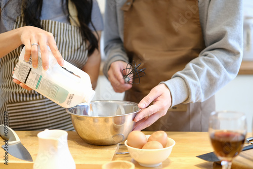 Woman hand pouring milk into mixed bowl, preparing dough for homemade pancake with her boyfriend