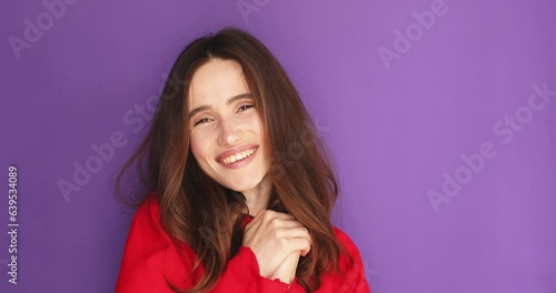 Brunette curly woman looking at camera charming smile, say oh it so sweet put hands. Girl wear red long sleeves isolated on purple background. Oh so sweet. Friendly or lovely look female. photo