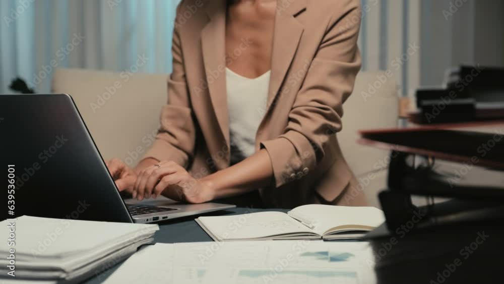 Tilt up shot of busy woman writing notes and using laptop while doing tasks before deadline in office at late nightTilt up shot of busy woman writing notes and using laptop while doing tasks before de Tilt up shot of busy woman writing notes and using laptop while doing tasks before deadline in office at late nightTilt up shot of busy woman writing notes and using laptop while doing tasks before de