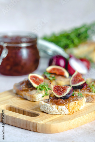 Homemade caramelized onion confit or marmalade on a slices of baguette with liver pate, figs and fresh thyme served on a wood serving board, selective focus. Healthy organic food.