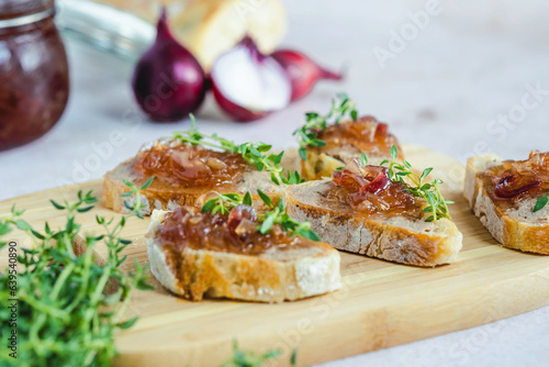 Homemade caramelized onion confit on a slices of bread with liver pate, fresh thyme, served on a wood serving board, selective focus. Healthy organic food photo