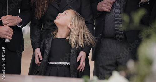 Mourning, grief and family with girl at funeral, flowers on coffin, death and sad child at service in graveyard. Support, loss and people at casket in cemetery with kid crying at grave for burial.