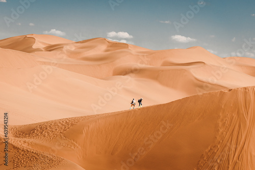 Two people hiking up a sand dune at Kumtag Desert  Xinjiang