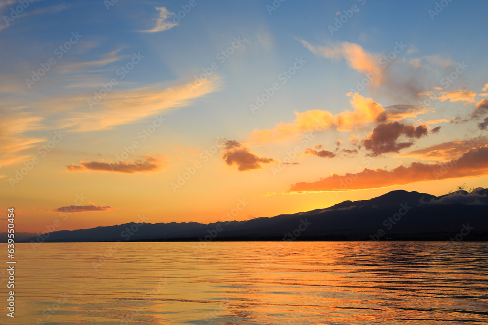 Colorful sunset on the sea. Mountain lake in the rays of the orange sun. Kyrgyzstan, Lake Issyk-Kul. Colorful sunset on the sea. Mountain lake in the rays of the orange sun. Kyrgyzstan, Lake Issyk-Kul.