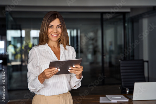 Latin Hispanic 40s years mature business woman looking at camera. smiling European businesswoman CEO holding digital tablet using fintech tab online application standing in modern office, copy space