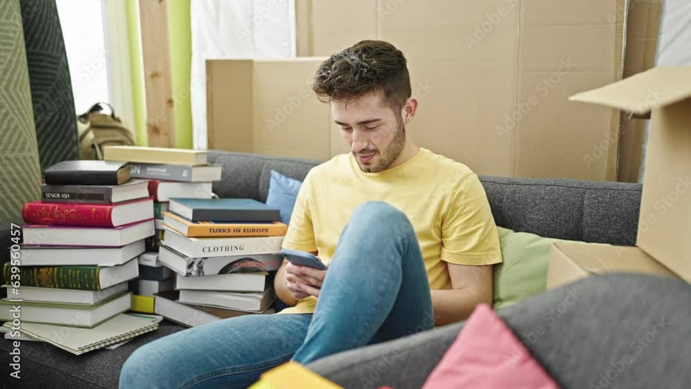 Young hispanic man using smartphone sitting on sofa celebrating at new home Young hispanic man using smartphone sitting on sofa celebrating at new home