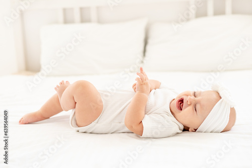 a crying little baby on a white bed at home, a sick child crying and screaming and calling for mom