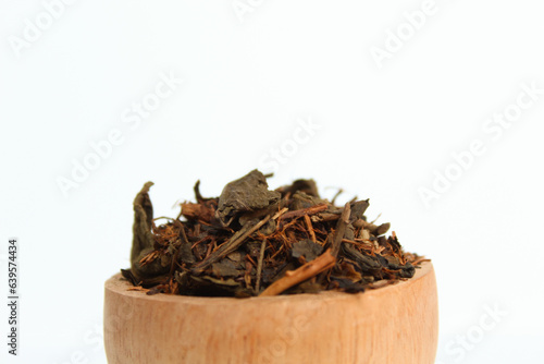 Dried black tea before brew, in a wooden bowl. Isolated on white background. Side view photo