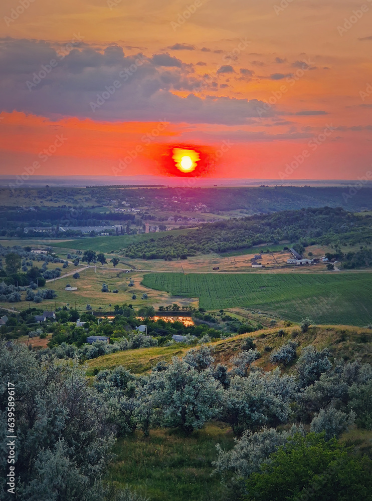 Fototapeta premium Red summer sunset scenic view over the green valley with bushes and trees. Evening natural landscape