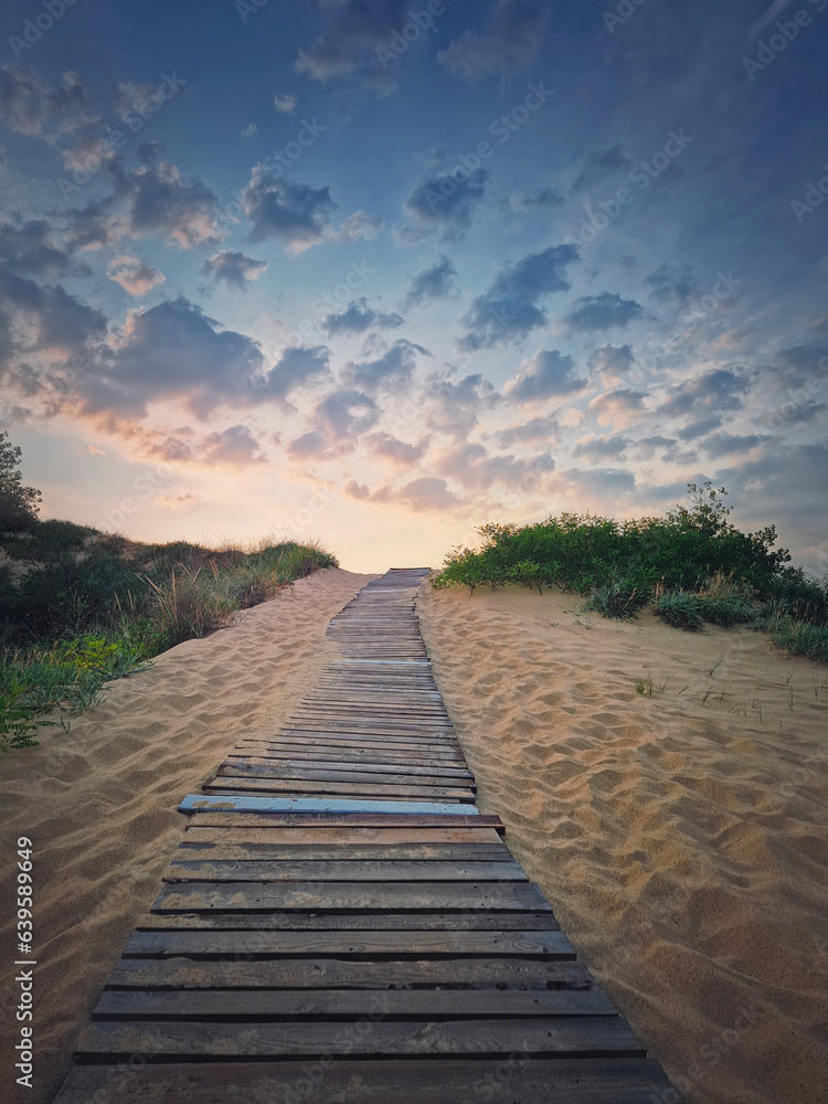 Wooden pathway through the sand leading to the beach. Beautiful morning sky with fluffy clouds