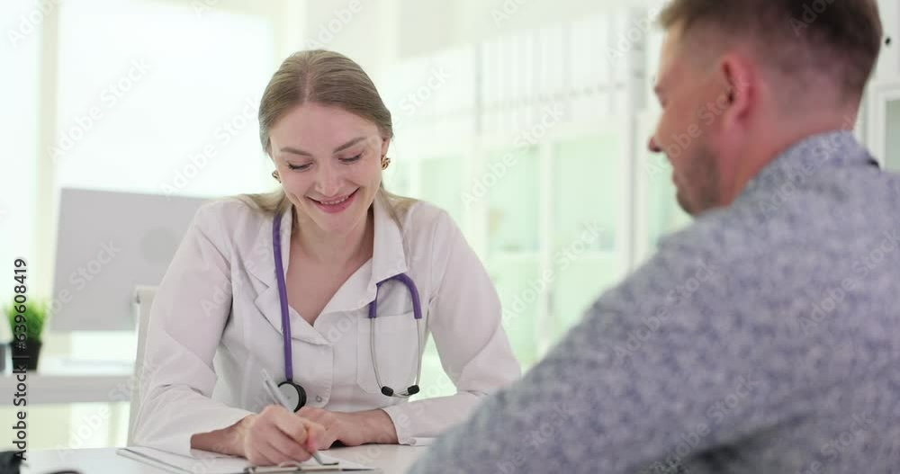 Smiling doctor writing down good health test result. Male patient discussing successful treatment of illness or health insurance Smiling doctor writing down good health test result. Male patient discussing successful treatment of illness or health insurance