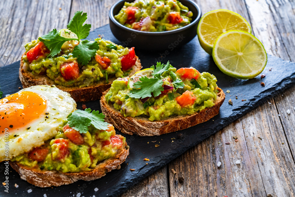 Tasty bruschetta with sunny side up egg, guacamole, tomato, and onion on wooden table
Tasty bruschetta with sunny side up egg, guacamole, tomato, and onion on wooden table