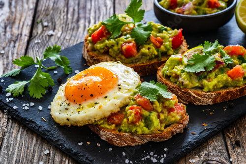 Tasty bruschetta with sunny side up egg, guacamole, tomato, and onion on wooden table
