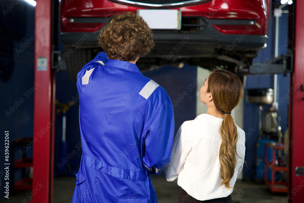 back view mechanic showing how to fix a car to businesswoman in automobile repair shop