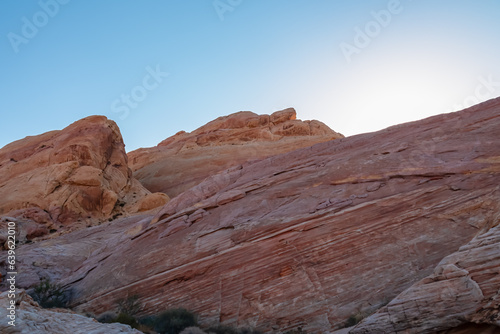 Scenic view on wall of striated red and white rock formations along the White Domes Hiking Trail in Valley of Fire State Park in Mojave desert, Nevada, USA. First sunlight touches arid landscape