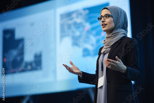 Arab Business Woman on stage at conference holding a presentation of a new product, Speaker having a lecture about digitization, engineering, sustainability, automation.