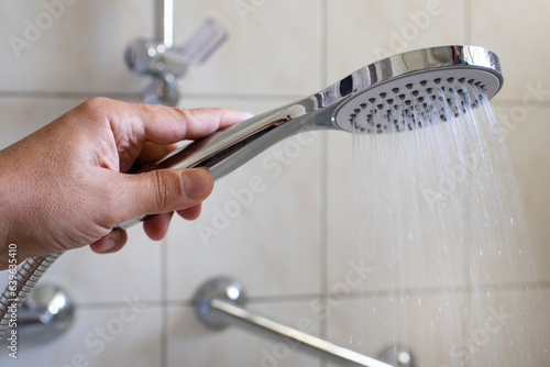 Shower head in a man's hand. Savings and problems with the supply of water. Taking a shower.