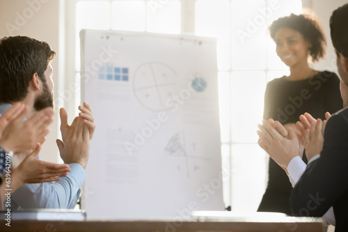 Close up of overjoyed diverse businesspeople clap hands greeting successful female coach or trainer at meeting, excited employees applaud thanking speaker for presentation, acknowledgement concept photo