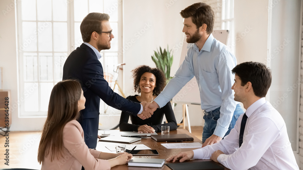 Smiling businessman stand at meeting shake hands get acquainted greeting in office, happy male business partners handshake close deal make agreement at briefing, acquaintance, partnership concept Smiling businessman stand at meeting shake hands get acquainted greeting in office, happy male business partners handshake close deal make agreement at briefing, acquaintance, partnership concept