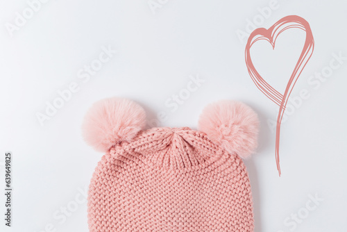 Pink knitted hat with pumpons on a gray background, top view. Children's cute hat on a light background with a heart photo