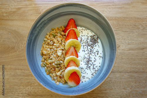 A parfait featuring layers of strawberries, bananas, granola, sunflower, yogurt seeds, and chia seeds, displayed on a rustic wooden background,  photo