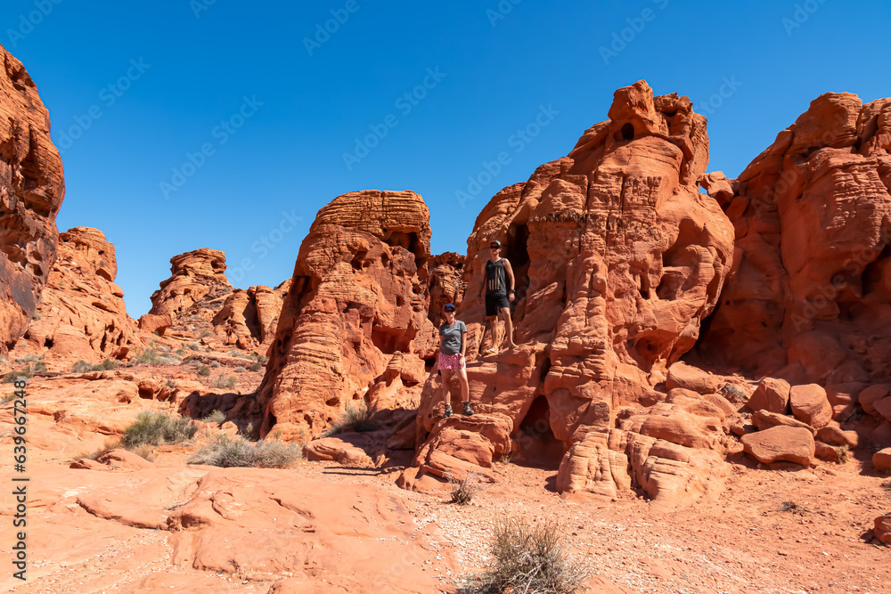 Couple at the entrance of windstone arch (fire cave) in Valley of Fire State Park, Mojave desert, Nevada, USA. Scenic view of beehive shaped red sandstone rock formations. Barren deserted landscape