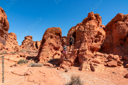 Couple at the entrance of windstone arch  fire cave  in Valley of Fire State Park  Mojave desert  Nevada  USA. Scenic view of beehive shaped red sandstone rock formations. Barren deserted landscape