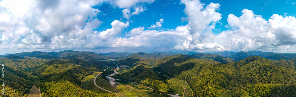 wide aerial panorama overlooking the mountain gorges in the forested mountains of the western caucasus (southern Russia) with clouds on a sunny summer day