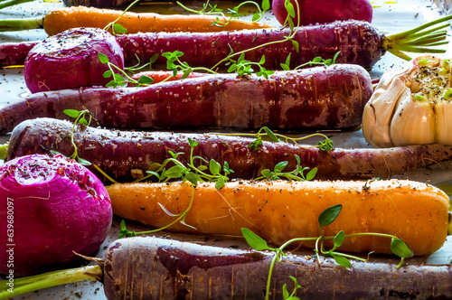 Purple and yellow roasted carrots with turnips and garlic on cooking tray. photo