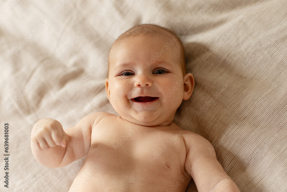 Adorable baby portrait, newborn caucasian child lying on bed at home, sweet infant boy or girl smiling at camera, above view Adorable baby portrait, newborn caucasian child lying on bed at home, sweet infant boy or girl smiling at camera, above view