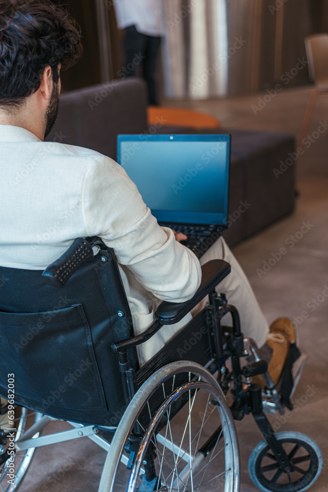 Back view photo of handicapped male employee in wheelchair working on lap top Back view photo of handicapped male employee in wheelchair working on lap top