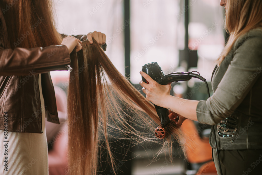 Naklejka premium Ginger female client helping professional hairstylist ironing a ginger hair extension.