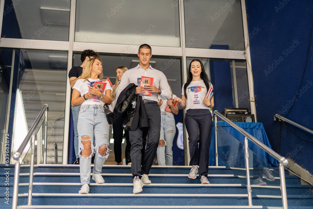 Obraz premium Happy, cheerful students going home after classes, walking downstairs, having a conversation and smiling
