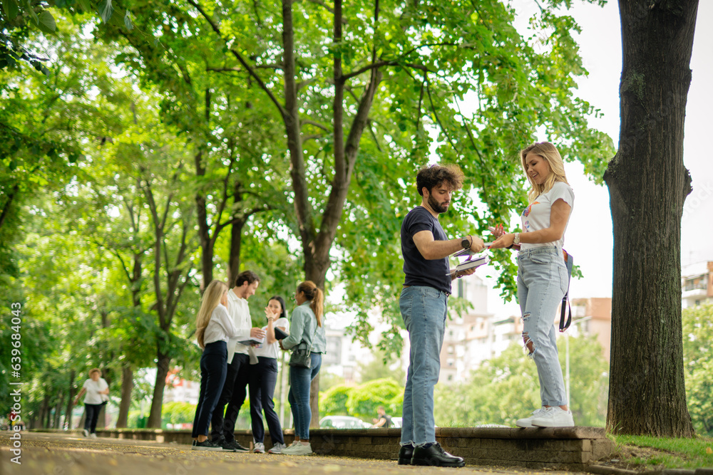 Lovely university couple helping each other before exam while standing on a pavement in the city Lovely university couple helping each other before exam while standing on a pavement in the city