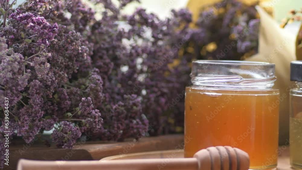fresh natural honey pouring in glass jar with wooden honey spoons around herb flowers fresh natural honey pouring in glass jar with wooden honey spoons around herb flowers