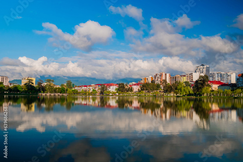 View of the blue sky with white clouds over modern apartment, residential buildings with reflection in the water surface. 6 May Park on the shore of lake in Batumi in the afternoon