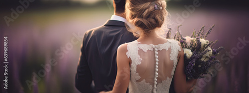 primer plano de espaldas de una pareja vestida de novios con un ramo de lavanda sobre fondo desenfocado de un campo malva