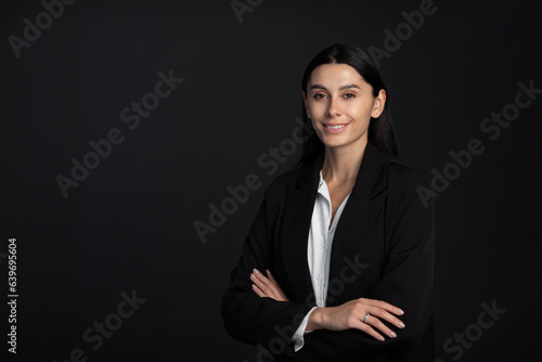 Close-up of an attractive business woman with toothy smile staning at isolated dark background, copy space.