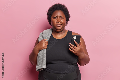 Obraz na płótnie Plus size obese curly woman has discontent expression wears black t shirt poses