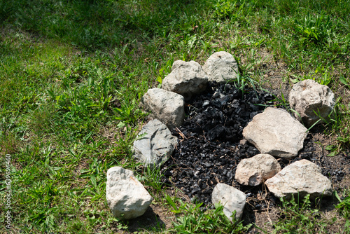 fire pit with river stones and brunt out charcoal on the grass in summer  
