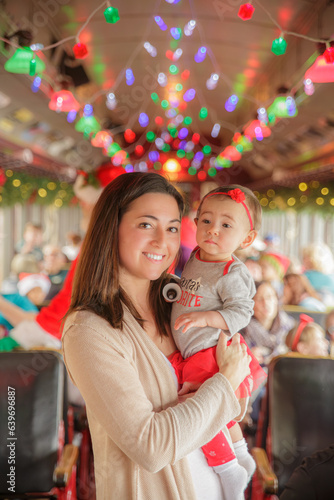 Mother holding beautiful baby girl with colorful christmas lights in the background on train or bus