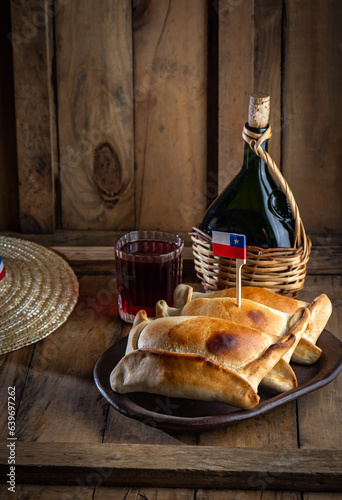 Chilean independence day concept. fiestas patrias. Tipical baked empanadas de pino, wine or chicha, hat and play emboque. Dish and drink on 18 September party, wooden background photo