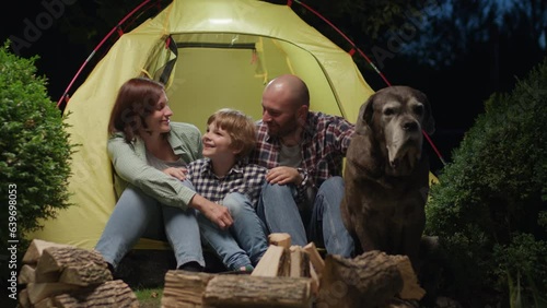 Family with Dog Sitting in Tent by Campfire at Night. Mom Dad and Son bumbing fists while camping together. photo