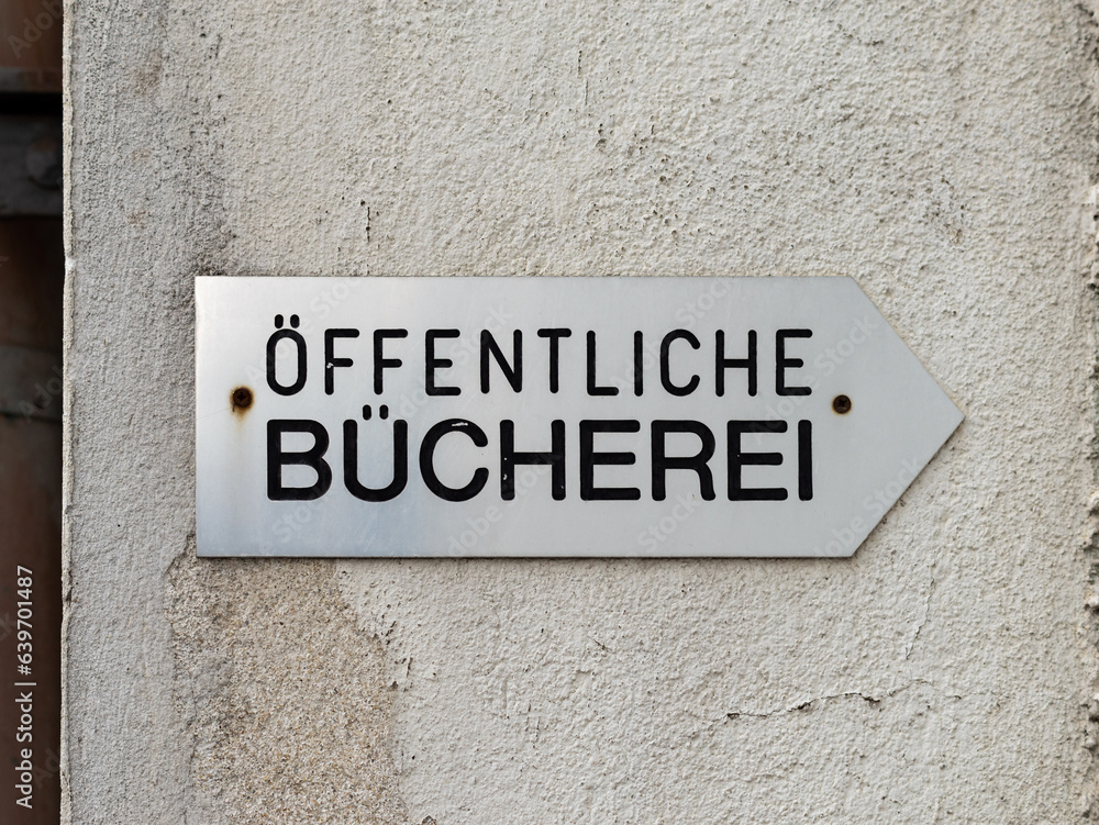 Öffentliche Bücherei (public library) sign with an arrow directing to the right. Building exterior wall with a weathered plaster. Öffentliche Bücherei (public library) sign with an arrow directing to the right. Building exterior wall with a weathered plaster.