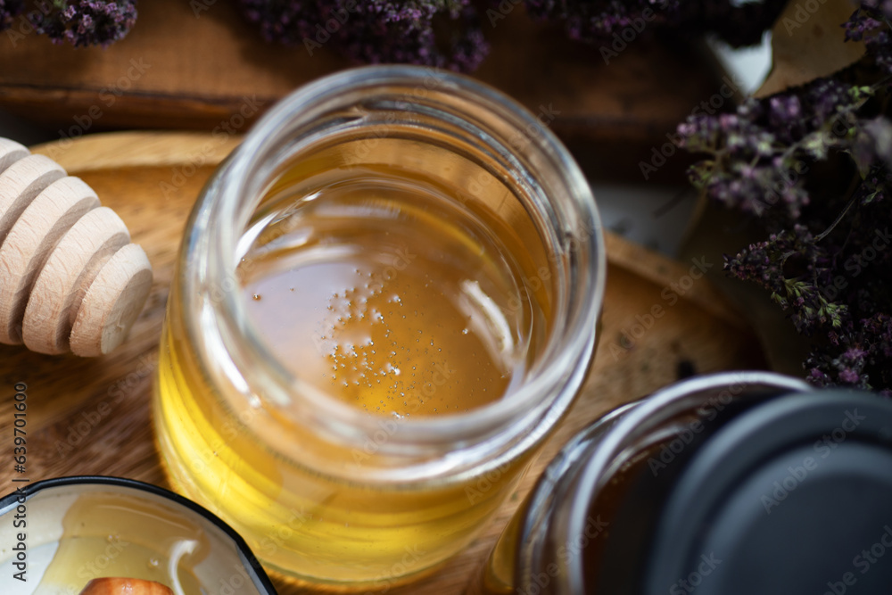 fresh natual linden honey in glass jar with wooden honey spoon around herb flowers. close up fresh natual linden honey in glass jar with wooden honey spoon around herb flowers. close up